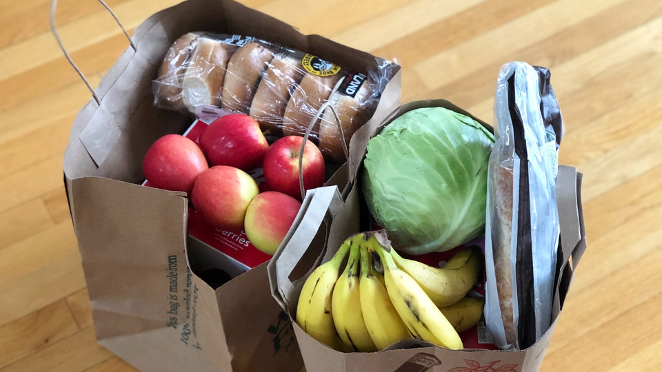 Två papperkassar med matvaror: äpplen, bananer, vitkål och bröd.