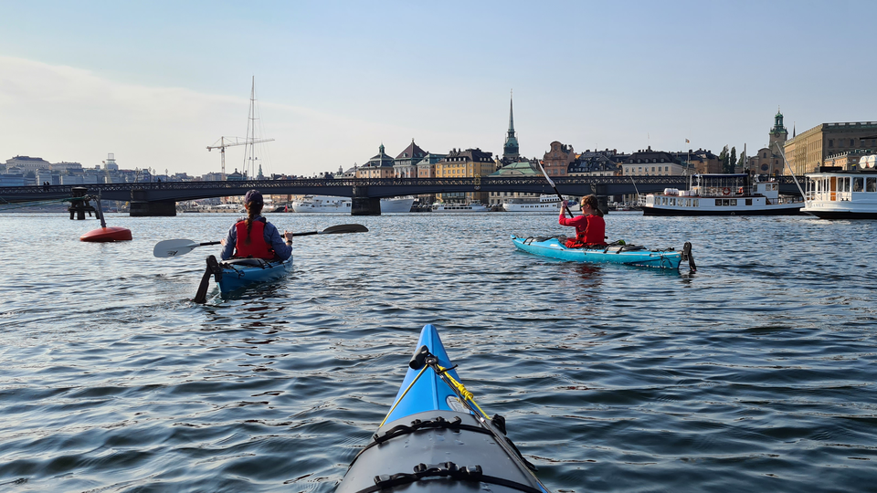 Two kayaks in the water i Stockholm, buildings, a church tower and some archipelago boats in the background.